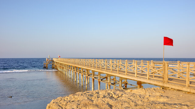 A wooden pier with a red warning flag at sunset.