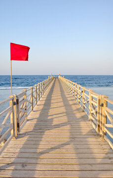 A wooden pier with a red warning flag at sunset.