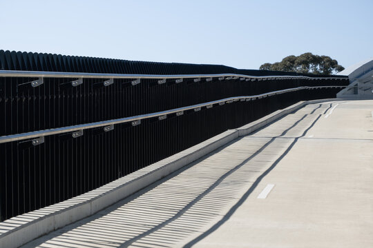 Modern pedestrian and bicycle ramp overpass featuring sleek stainless steel double handrails, dark vertical security fencing,&nbsp;and a clean concrete path&nbsp;on Federation Trail, Melbourne Australia
