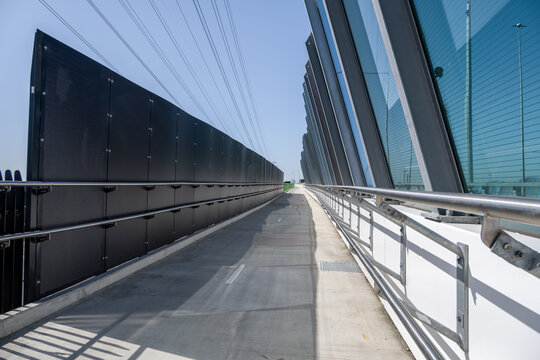 An elevated section of the Federation Trail shared-use overpass, framed by high dark barrier panels on the left and glass acoustic screens with steel handrails. Melbourne, Australia