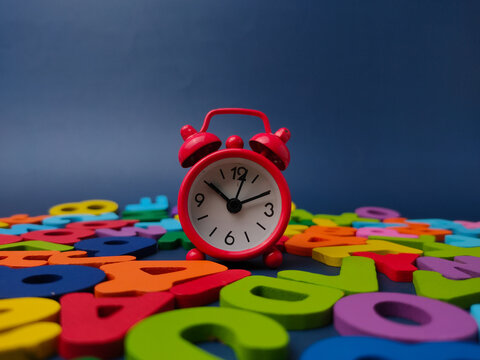 Small red twin bell alarm clock stands upright on a field of colorful wooden letters and numbers