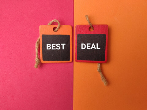 Two wooden hanging tags labeled BEST and DEAL resting on a pink and orange split background