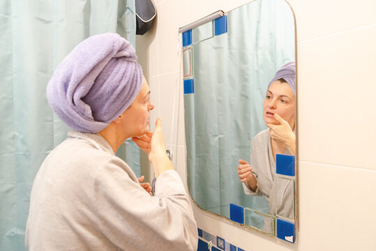 Young Woman with Towel Turban Doing Skincare Routine in Bathroom Mirror