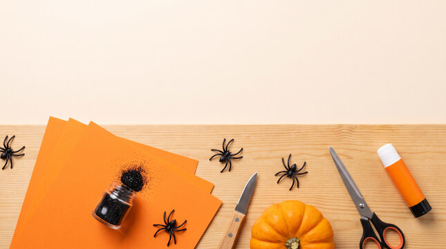 Festive Halloween Crafting Supplies on a Wooden Table Featuring Orange Paper, a Pumpkin, Scissors, Glue, and Decorative Spiders for Creative Seasonal Projects, copy space