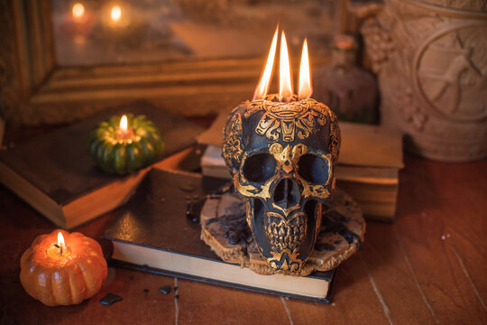 Maya carved skull candle with burning flames on old spell book, pagan ritual altar and esoteric concept 
