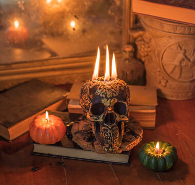 Maya carved skull candle with burning flames on old spell book, pagan ritual altar and esoteric concept 