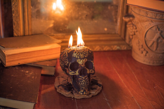 Maya carved skull candle with burning flames on old spell book, pagan ritual altar and esoteric concept 