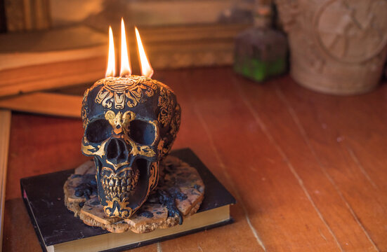 Maya carved skull candle with burning flames on old spell book, pagan ritual altar and esoteric concept 