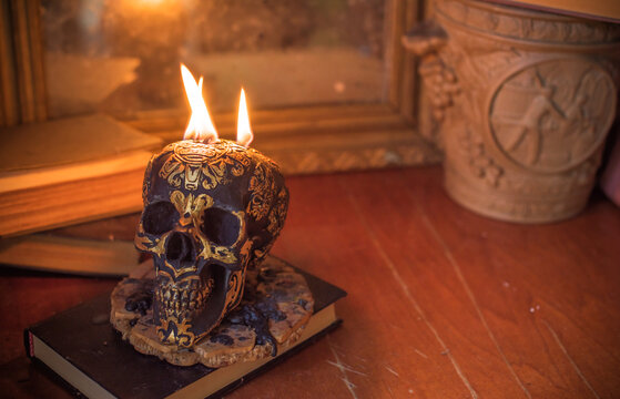 Maya carved skull candle with burning flames on old spell book, pagan ritual altar and esoteric concept 