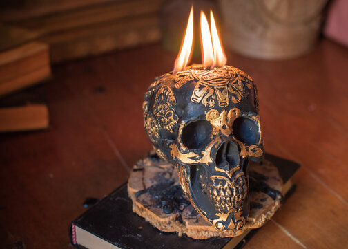 Maya carved skull candle with burning flames on old spell book, pagan ritual altar and esoteric concept 
