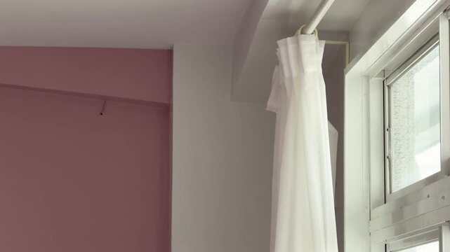 cinematic shot of a gentle white sheer curtain by a window with natural bright light against a modern pastel pink and white wall interior