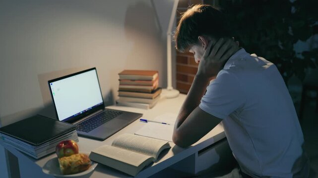 Sleepy teen boy resting his head on the home desk near the laptop.