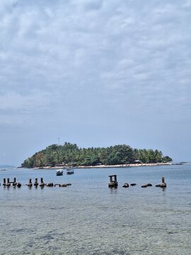 Tropical island landscape featuring lush green palm trees and historic pier ruins in calm blue ocean waters