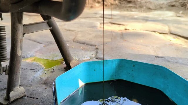 detailed shot of used black engine oil flowing out of a motorcycle's drain plug during a service 