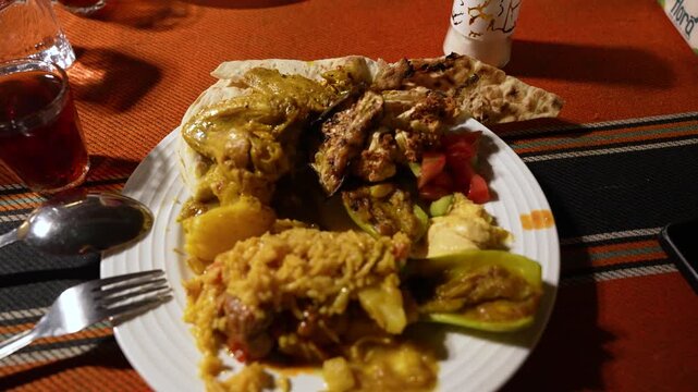Close-up of a Jordanian buffet plate with grilled chicken, seasoned rice, hummus, flatbread, stuffed vegetables and fresh salad on a restaurant table.