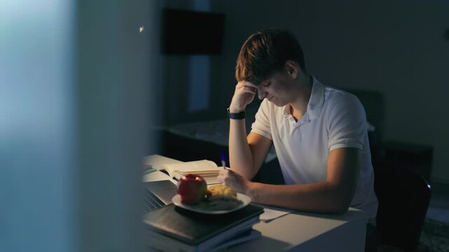 Overworked teenager crying at the dark study desk during a late learning session.