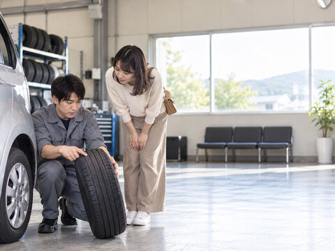 外したタイヤを見せながら女性客に説明する整備士