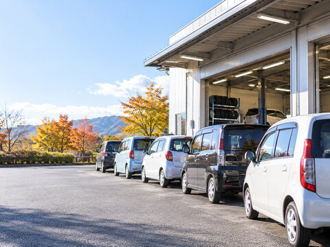 紅葉した山を背に整備工場の前へ並ぶ軽自動車