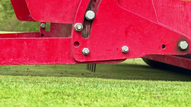 Ground-level close-up shows a turf aeration machine puncturing the soil with metal tines before a rear roller passes over the grass.