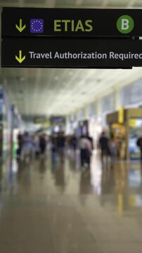 Airport sign indicating the new ETIAS travel authorization required for entering the European Union, with blurred people walking in the terminal corridor in the background