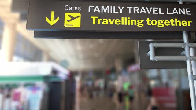 Airport sign indicating the family travel lane for passengers travelling together with children, with a blurred background of a busy terminal showing people walking towards the departure gates