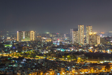 Fototapeta premium A panoramic view of a densely built urban skyline illuminated by streetlights and building windows beneath a dark night sky.