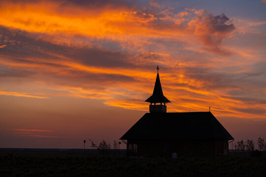Silhouette of wooden church in open field under vibrant orange sunset sky.