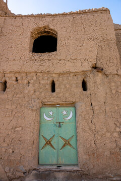 Green metal door decorated with crescent moon and star motifs set into a mudbrick facade, Ad Dakhiliyah Region, Al Hamra, Oman