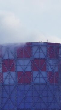 Vertical video shot of a tall red and white striped factory smokestack emitting dense white steam and emissions into a clear blue sky