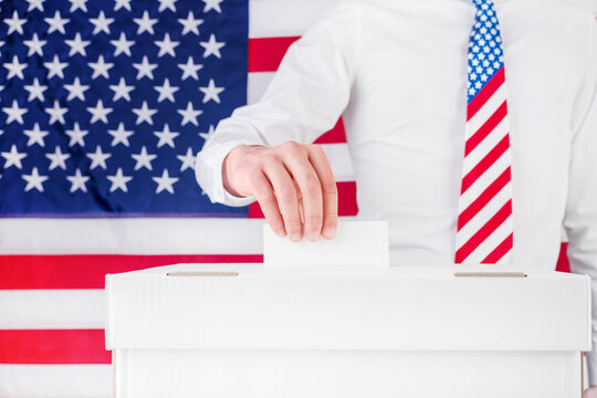 Voter in a patriotic necktie casts a blank ballot before an American flag