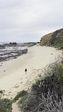 A happy girl runs along the empty Gunnamatta Beach, with stunning rock pools, raw cliffs and waves, near Cape Schanck, Mornington Peninsula, Melbourne, Victoria, Australia.