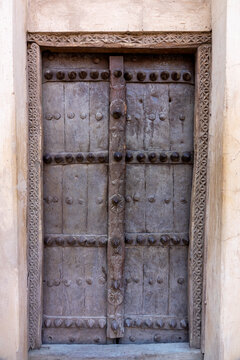 Weathered wooden door with decorative metal studs set in a carved mudbrick doorway, Ad Dakhiliyah Region, Nizwa, Oman