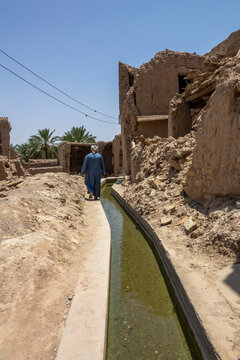 Man in a blue dishdasha walking along a falaj water channel through the ruins of the old village, Ad Dakhiliyah Governorate, Birkat Al Mouz, Oman