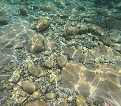 Vue sous-marine naturelle de reflets de lumi&egrave;re sur des rochers et galets &eacute;clair&eacute;s par les motifs lumineux du soleil dans une eau transparente et claire 