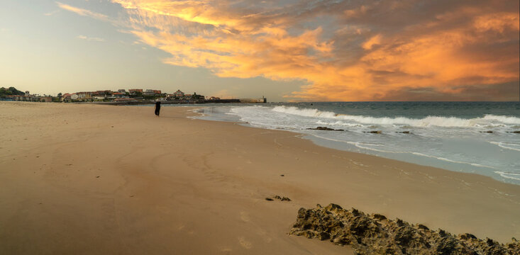Person walking along comillas beach at sunset
