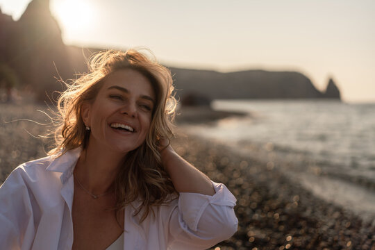 Woman beach golden hour, smiling young woman enjoying a happy carefree summer sunset on a pebble beach by the sea