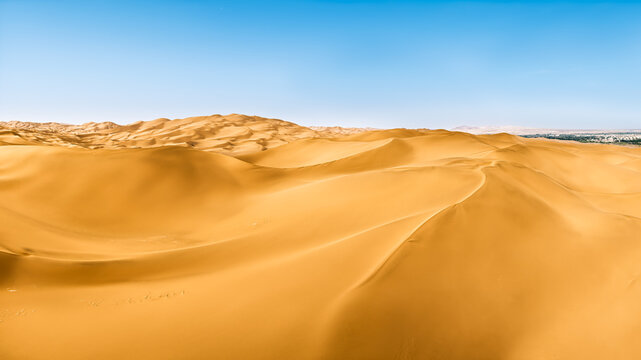 Rolling golden sand dunes under a clear blue sky in the Kumtag Desert, showing curved ridges in bright sunlight.