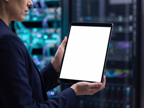 specialist in suit holding tablet with blank white screen mockup in front of server room background with flashing lights and cables