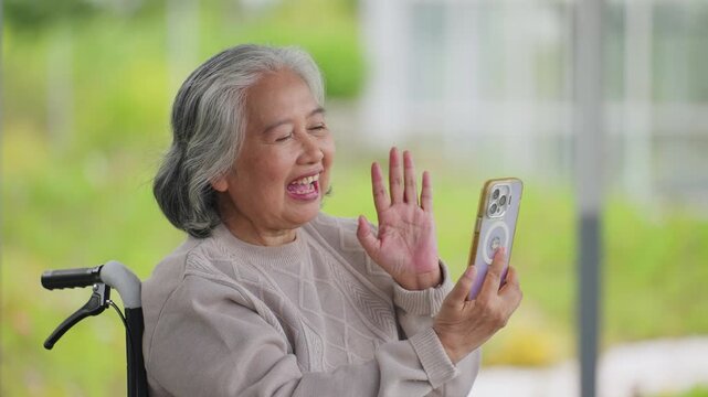 Senior woman smiles warmly while holding a phone. She sits comfortably in a wheelchair. Her expression shows joy and engagement