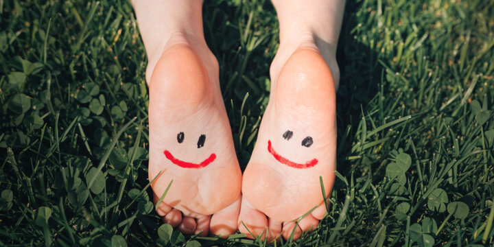 Lifestyle Positivity. Good mental health and relaxing on a holiday with feet that have smiles painted on them lying on the grass