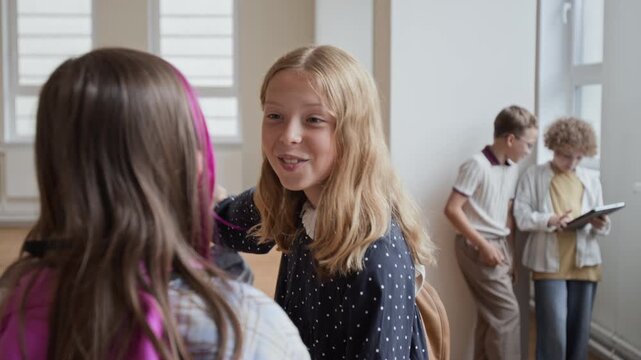 Caucasian schoolgirl hugging classmate and talking actively in school hallway. Clip serves back-to-school marketing, educational campaigns, and youth friendship storytelling