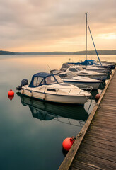 Fototapeta premium Leisure travel and vacation lifestyle, motorboats moored at a wooden pier on a calm lake during a peaceful golden hour sunset in the countryside
