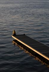 Fototapeta premium Solitude and tranquility, wooden pier extending into calm lake water at sunset with a yellow mooring buoy for peaceful nature and travel relaxation