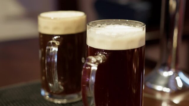 Two glasses of dark beer with creamy foam on bar counter in warm pub atmosphere
