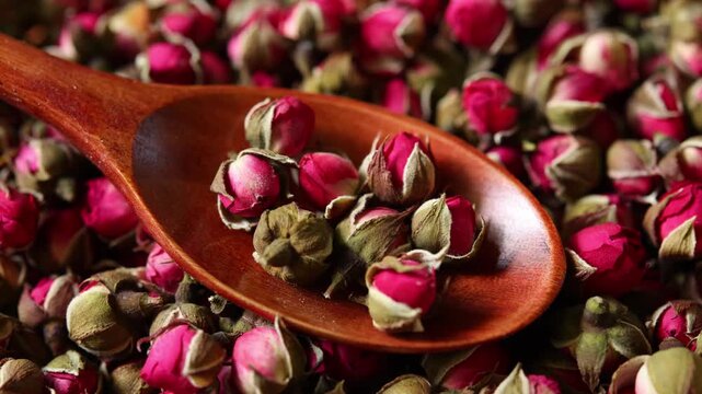 Dried rose flowers arranged in a natural wooden spoon, prepared as an ingredient for brewing herbal tea and showcasing their delicate peta