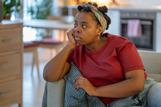 Tired african american woman rests head on hand while sitting alone at home, looking tired, bored, unmotivated. Everyday moment of fatigue, low energy, emotional exhaustion, apathy, lack of motivation