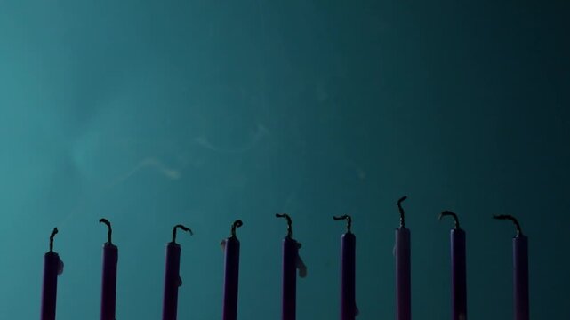Nine metallic pink and purple birthday candles burning in a row against a dark blue background, isolated. Happy Birthday card design concept.  Bottom lower border edge a lot of copy space. 
