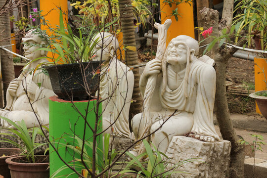 White marble Arhat Lohan statue holding carved wooden staff, traditional Buddhist ascetic disciple sculpture in monastery garden