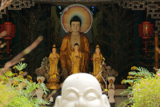 Golden Amitabha Buddha statue with colorful rainbow aura halo at Buddhist altar triad inside traditional temple shrine sanctuary