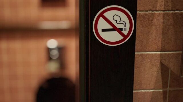 No smoking sign mounted on dark door beside tiled wall in softly blurred interior